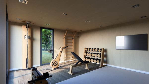 Salle de sport moderne et lumineuse, aménagée dans un module en bois avec des équipements en bois naturel : vélo d'intérieur, banc de musculation, rack d'haltères et mur d'exercice. Une grande baie vitrée offre une vue sur la nature environnante.